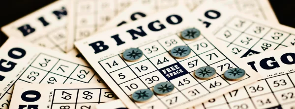 A close-up of several bingo cards, with one card in the center marked by blue bingo chips, including the free space in the middle—a classic scene from a Michigan Charitable Gaming event. Other bingo cards are scattered around underneath.