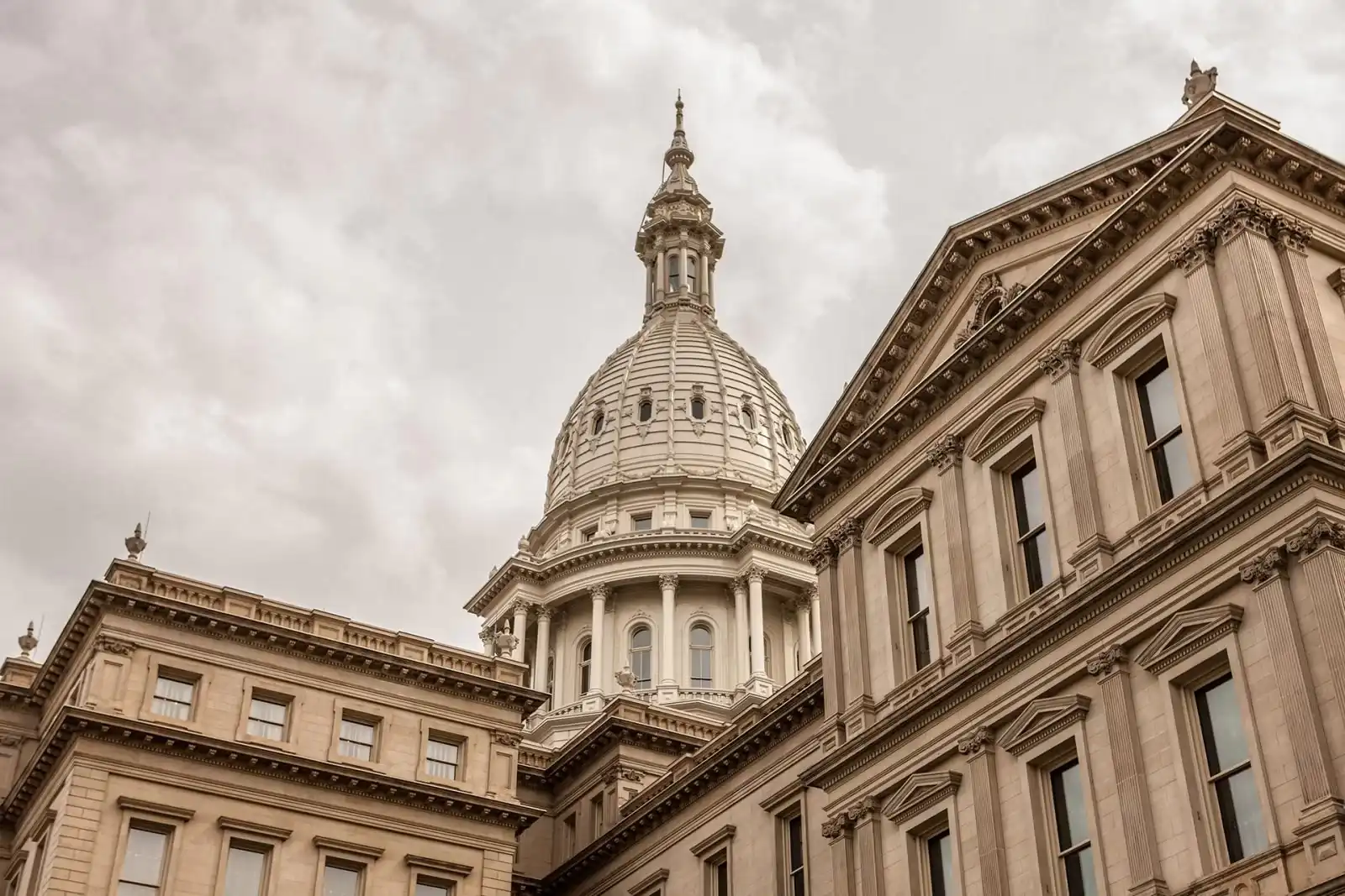 A close-up view of a historic government building with a large domed roof and intricate architectural details, set against a cloudy sky.